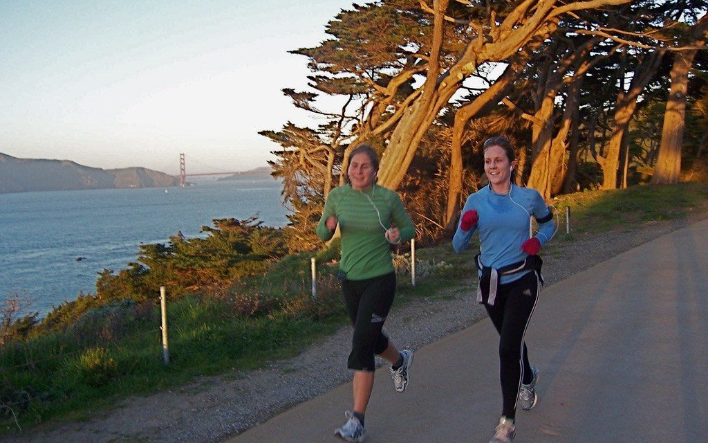 Heather and a friend running the Lands End trail at golden hour, the Golden Gate Bridge across the water behind them