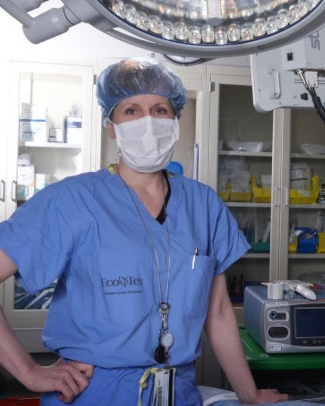Heather in scrubs, cap, and mask beneath an operating-room light