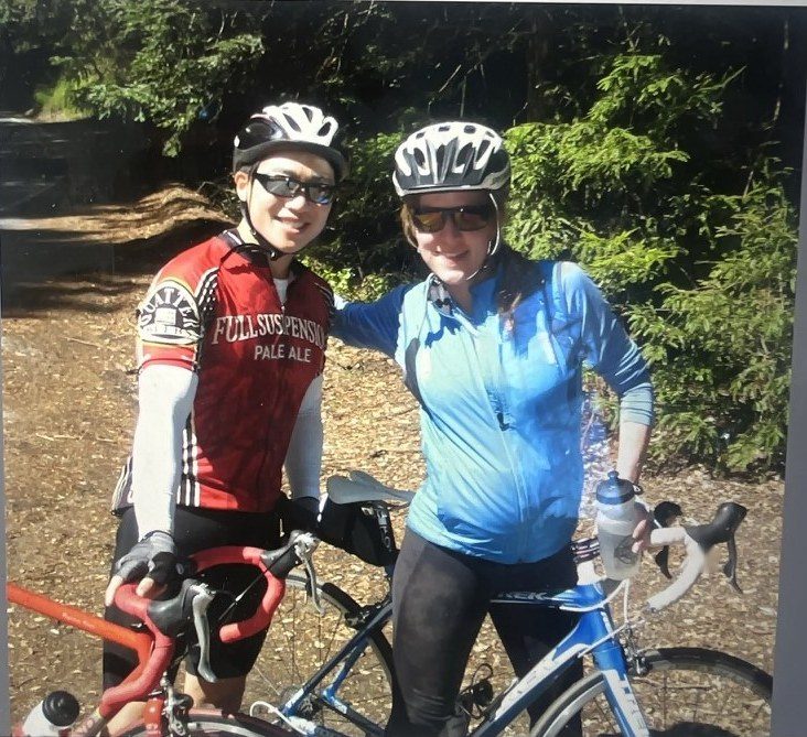 Heather, 38 weeks pregnant, in a blue cycling jacket and helmet with a friend and their road bikes at the top of Old La Honda Road