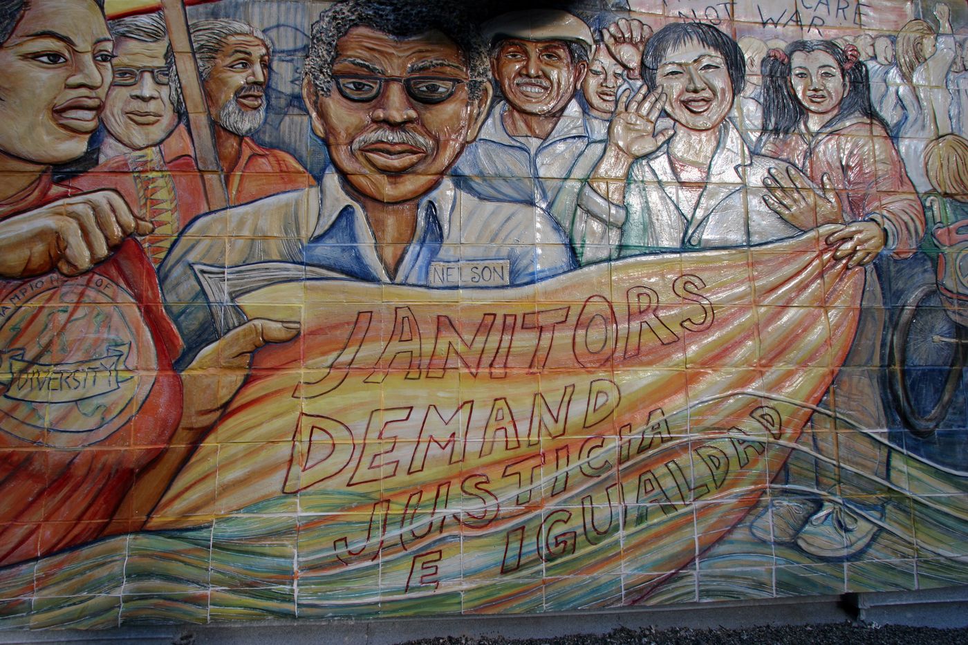 Detail of Juana Alicia&rsquo;s ceramic bas-relief mural &iexcl;Strike! at UCSF: marchers, among them a man in glasses with a NELSON name tag, carry a banner reading &ldquo;Janitors Demand Justicia e Igualdad.&rdquo;