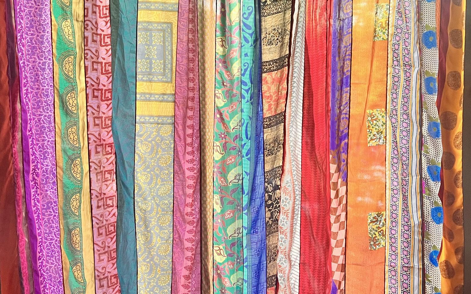 Hanging lengths of patterned sari fabric in violet, teal, gold, and coral