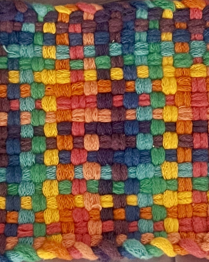 A hand-woven potholder, a grid of bright wool loops in orange, teal, violet, green, and gold