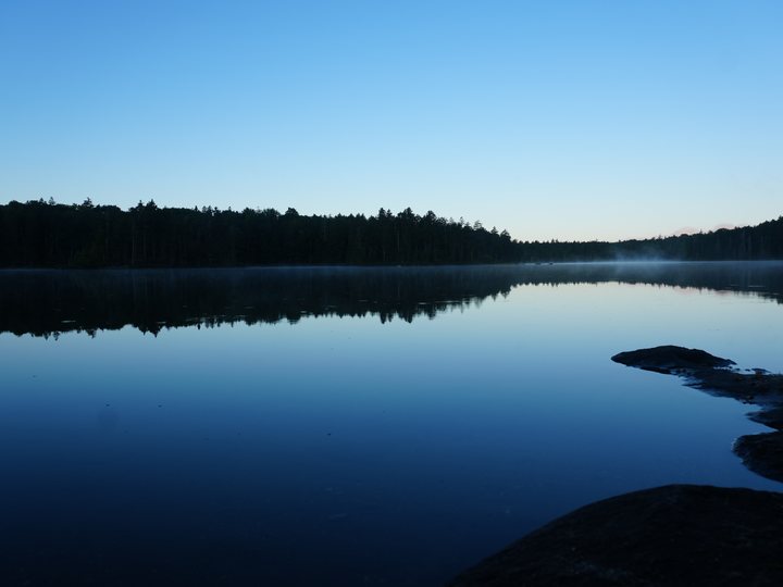 A still lake at dusk, the far shore of forest reflected in the water